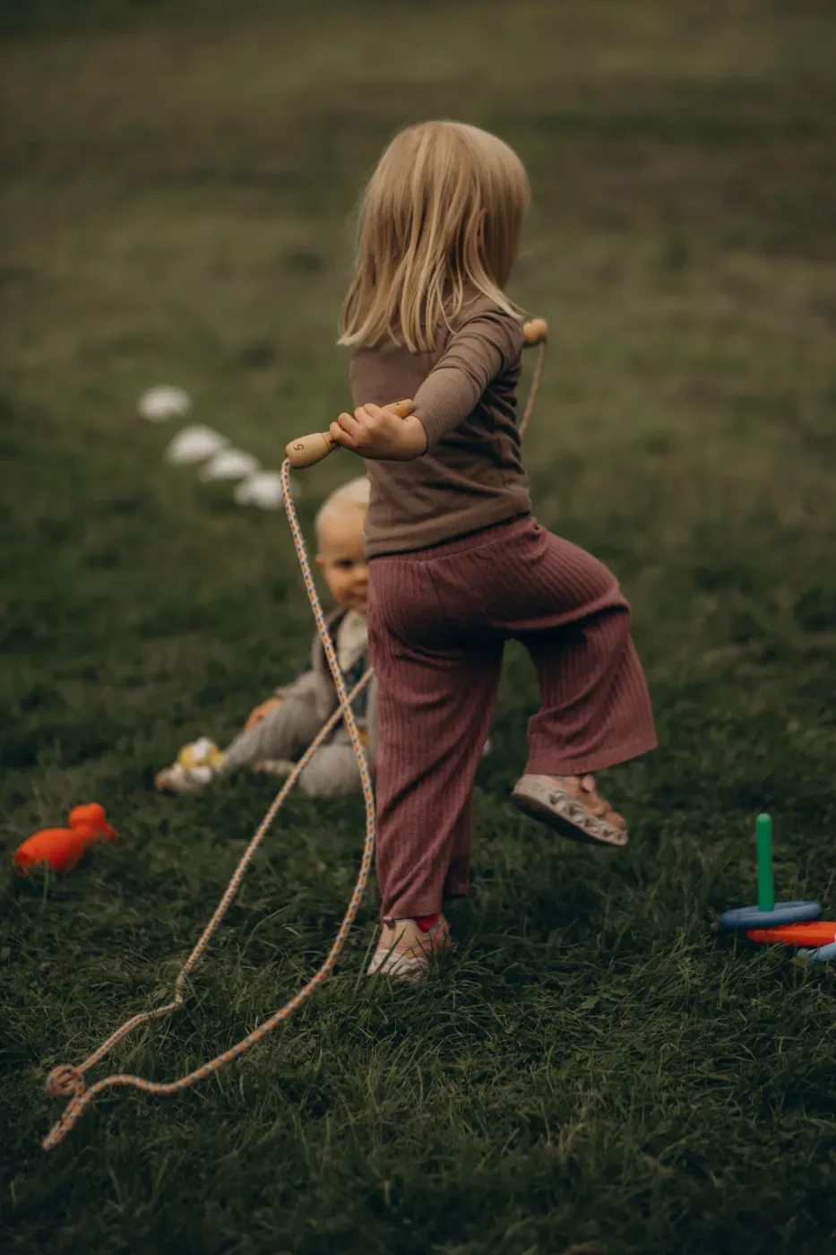 Ett barn klättrar över ett rep på en gräsplan medan ett annat barn sitter bakom och leker.
