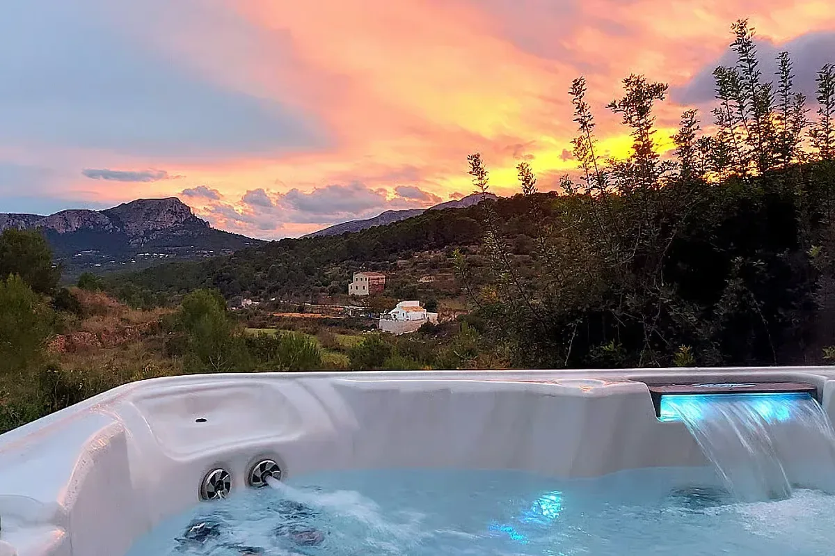 Jacuzzi med utsikt över bergslandskap i färgstark solnedgång