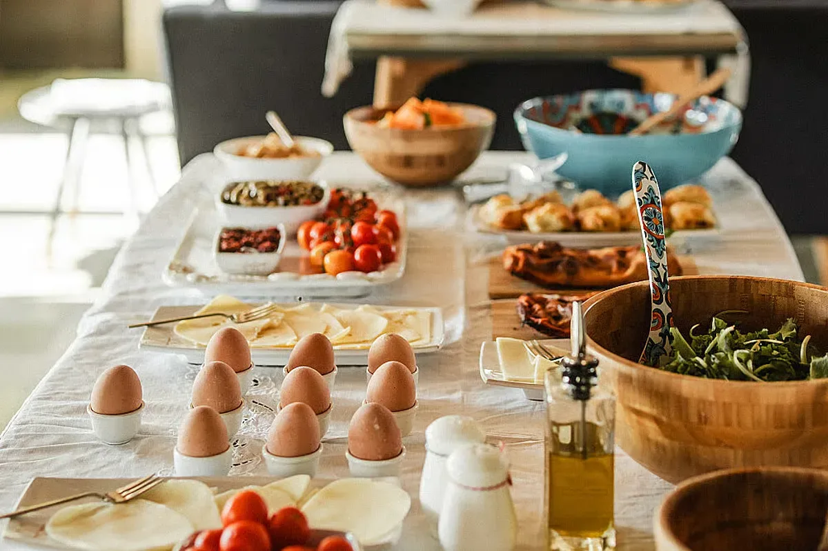 Ett dukat frukostbord med löskokta ägg, bröd, ost, tomater, sallad och flera skålar med tillbehör.