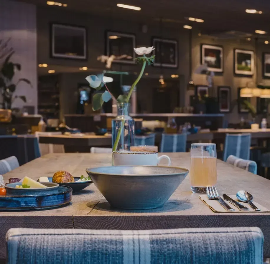 Ett dukat matbord med skålar, kopp, glas och en vas med blommor i en restaurangmiljö.