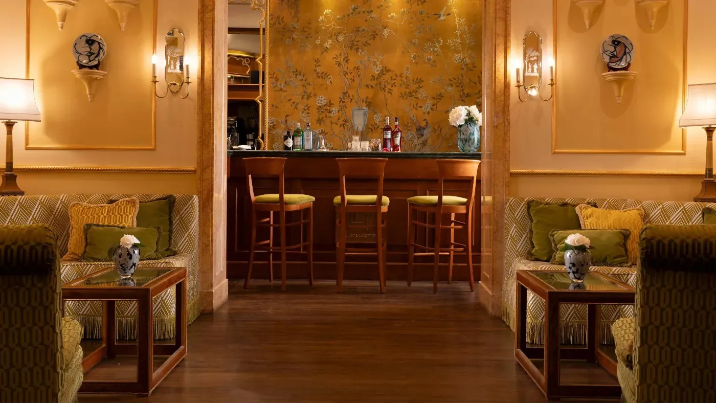 Elegant hotellounge med mönstrade soffor, fåtöljer, sidobord och en bar med tre höga stolar.