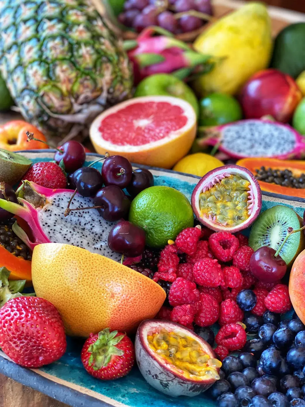 Ett fat med färsk ananas, citrusfrukter, drakfrukt, passionsfrukt, jordgubbar, körsbär, hallon och blåbär.