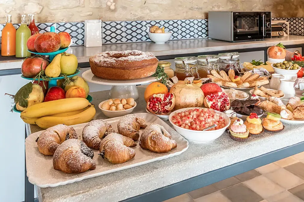 Ett dukat köksbord med sockerkaka, croissanter, frukt, granatäpplen, bakverk och burkar med tillbehör.
