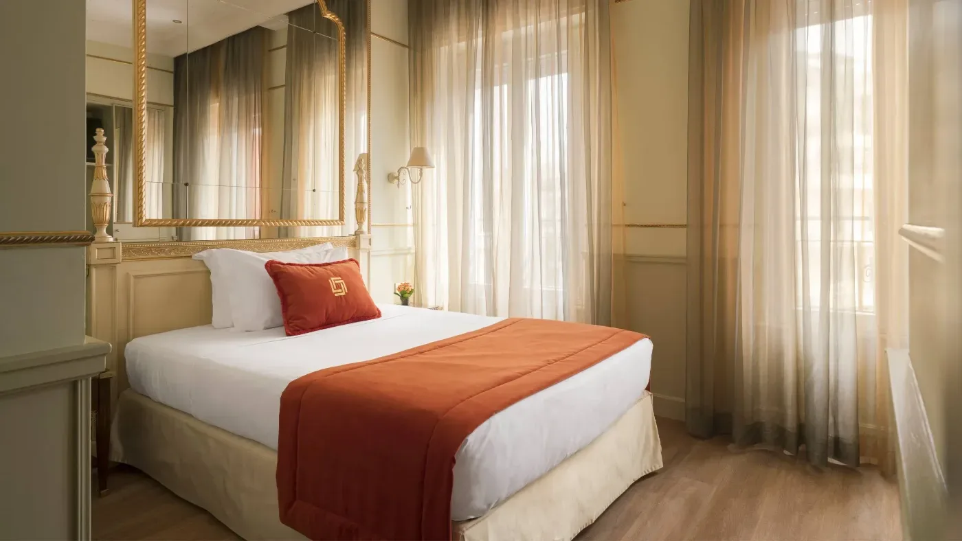 Ljust hotellrum i Rom med en bäddad dubbelsäng, terrakottafärgat överkast, stora speglar och höga fönster med tunna gardiner.