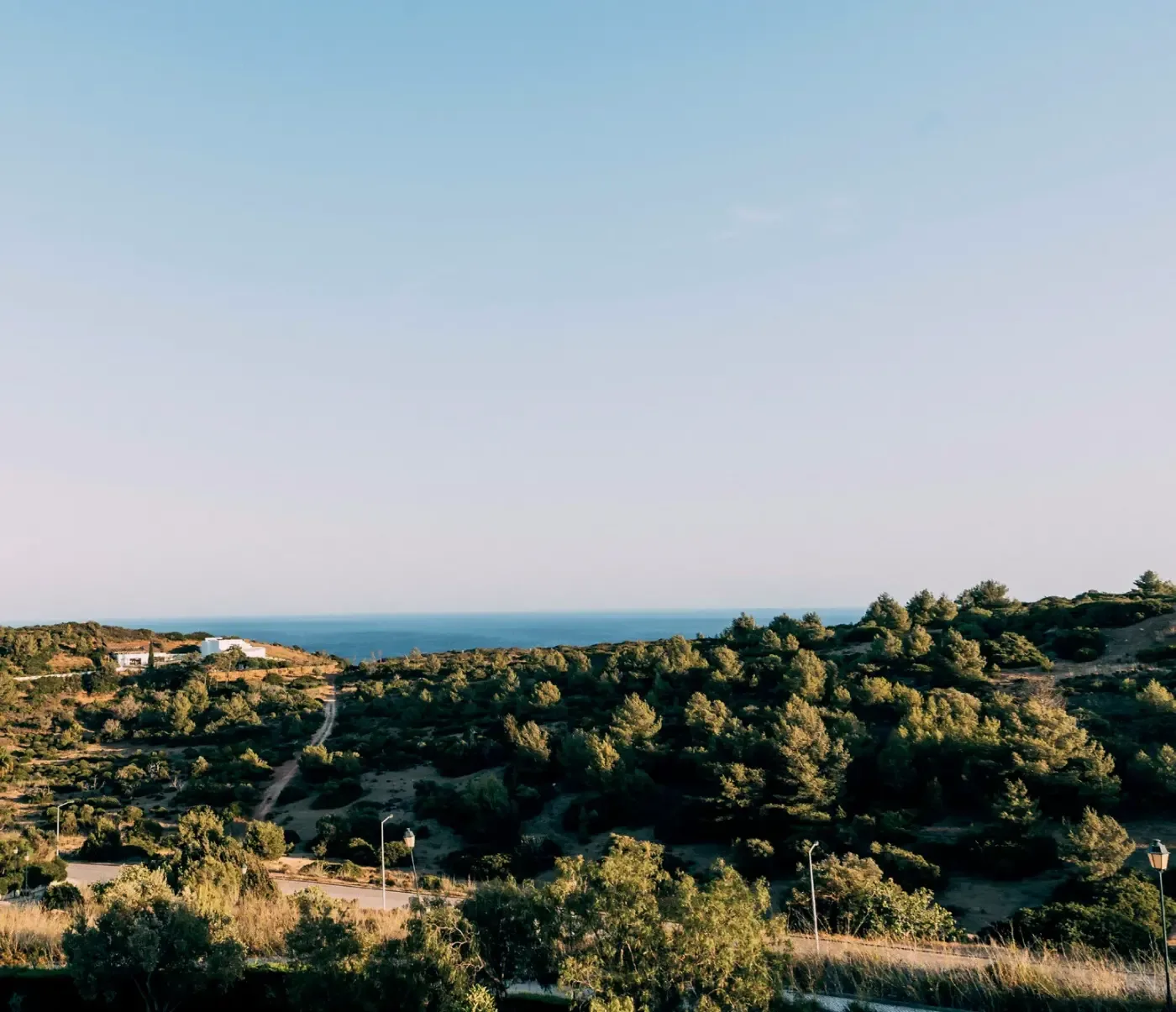 Kustlandskap i Algarve med tät grön vegetation, små vita hus, vägar och havet i bakgrunden under en klar himmel.