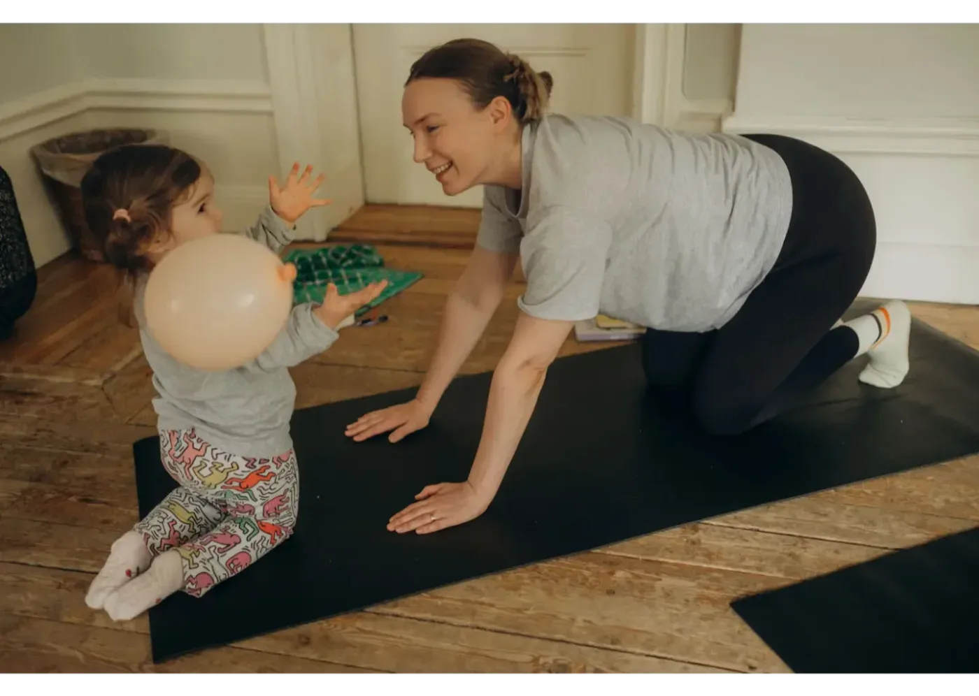 En mamma och ett barn leker tillsammans på en yogamatta inomhus.