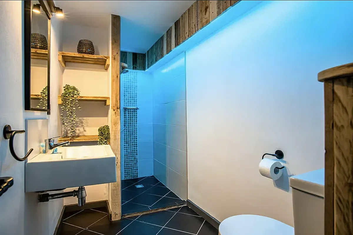 Modernt badrum med handfat, dusch med blå mosaik och trädetaljer.