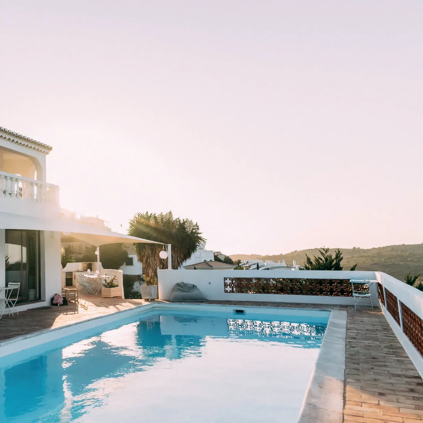 En solbelyst terrass med swimmingpool, vita byggnader och palmer mot ett kuperat landskap i Algarve, Portugal.