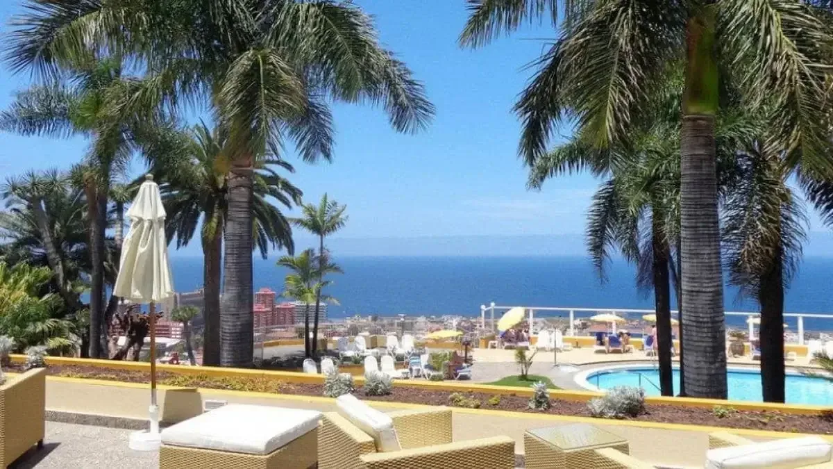 Poolområde med solstolar och palmer, med utsikt över havet och Puerto de la Cruz.