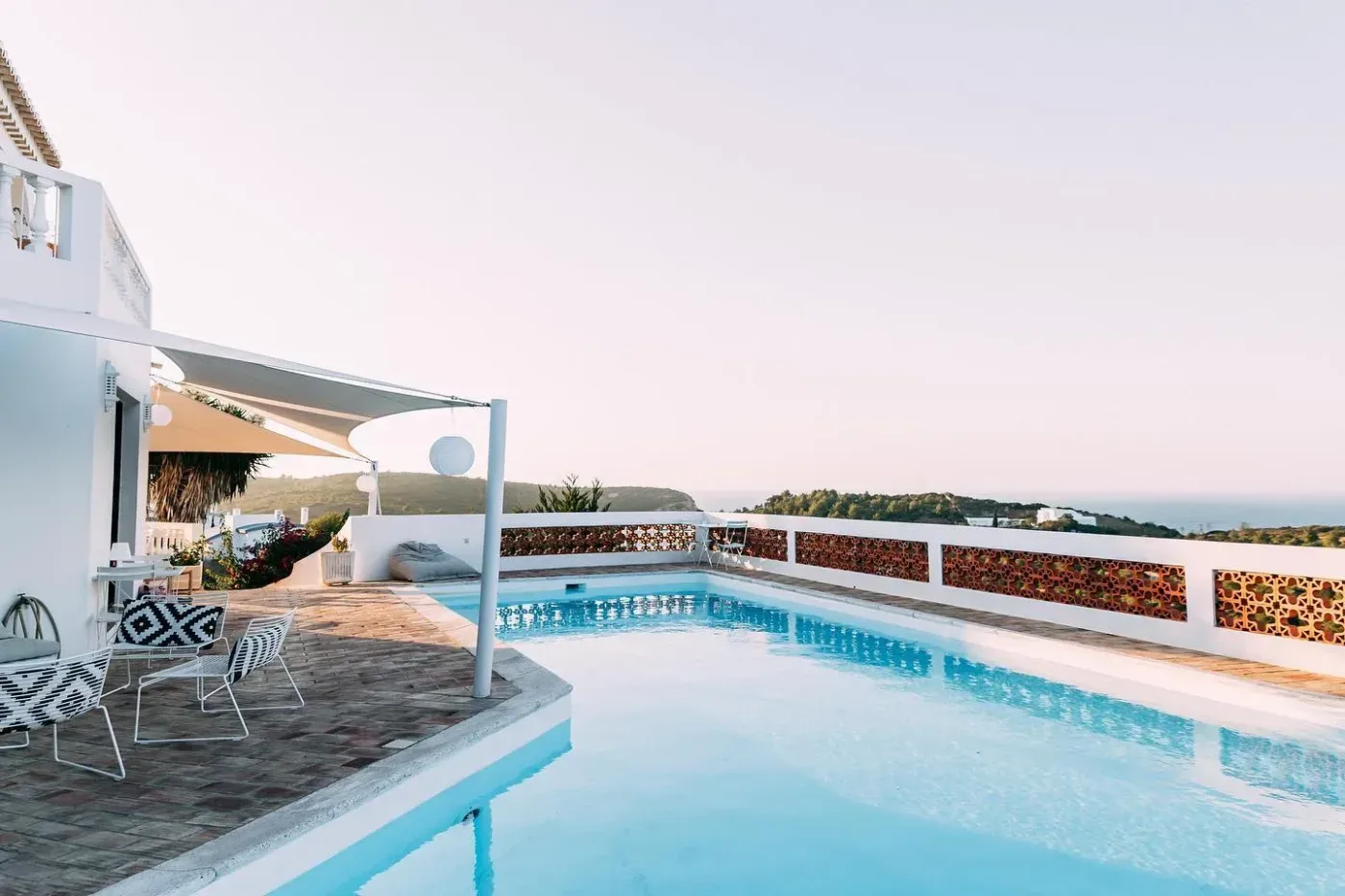 En solig terrass med pool, sittplatser och utsikt över Algarves kustlandskap i Portugal.
