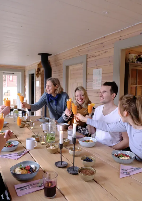 Fyra personer sitter runt ett dukat träbord och skålar med orange drycker i en ljus trästuga.