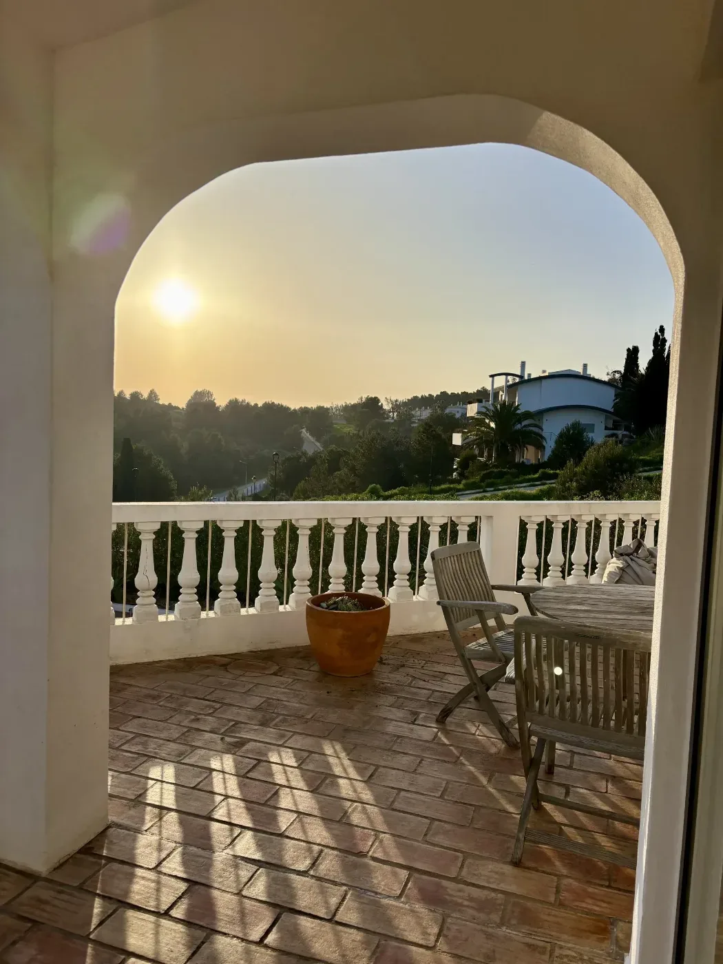 En solbelyst terrass med vita räcken, sittmöbler och utsikt över grönska och byggnader i Algarve.