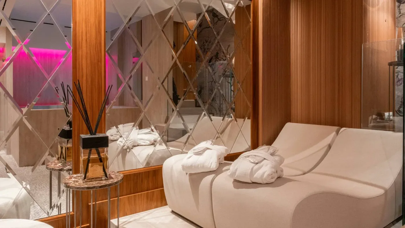 Ett elegant spa med två vita vilstolar, hopvikta badrockar, träpaneler och diamantformade speglar.