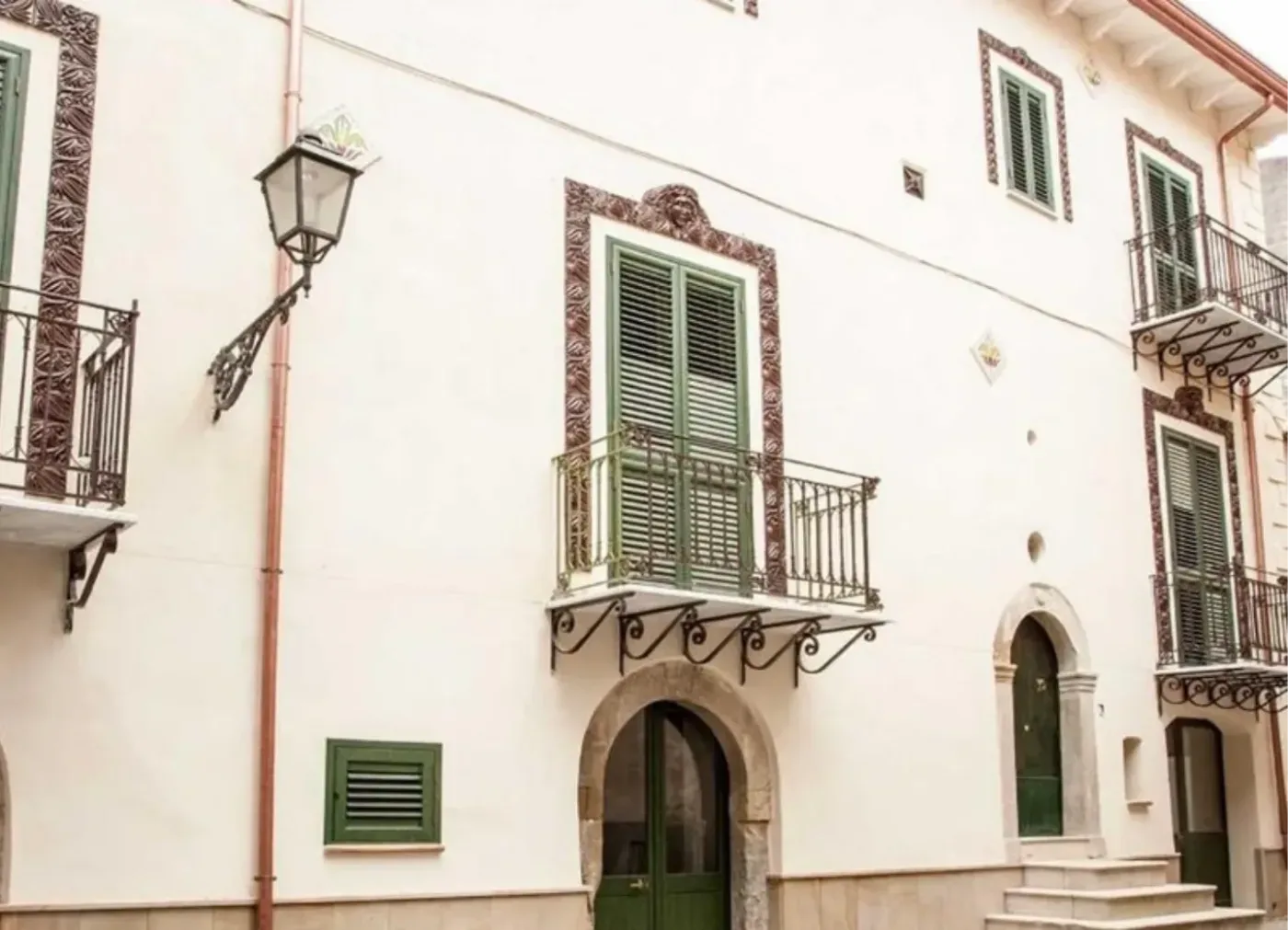 Ljus stenbyggnad i Santo Stefano di Camastra med gröna fönsterluckor, smidesbalkonger och välvda dörrar.