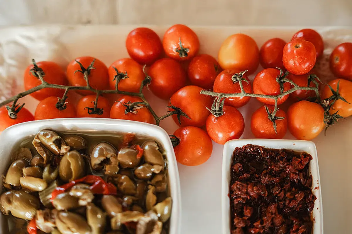 Röda tomater på kvist ligger tillsammans med två skålar med marinerad svamp och mörk tomatröra.
