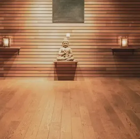 Ett varmt träklätt rum med en liten Buddhastaty på en vägghylla, omgiven av två tända lyktor.