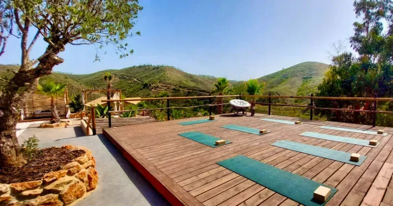 En trädäckad uteplats med yogamattor och träblock, omgiven av grönskande kullar i Algarve.