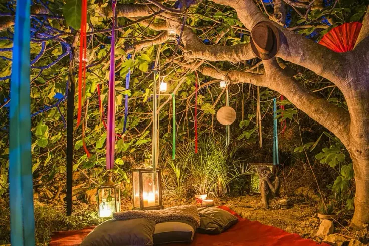 Stämningsfull meditationsplats utomhus under ett träd med lyktor och kuddar